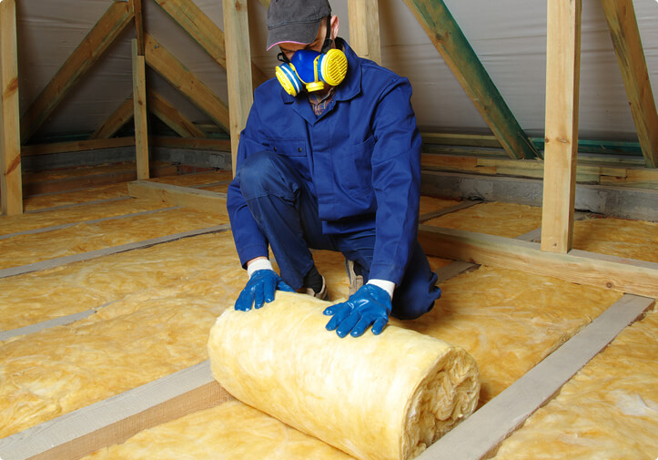 Man with proper PPE rolling insulation in an attic
